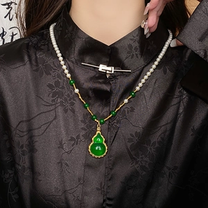 Detail of a natural pearl necklace with green hulu pendant and gold plated metal