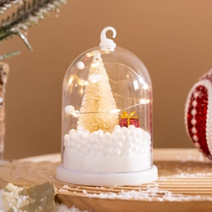 Close-up of a warm LED Christmas tree light with mini gift box and faux snow inside