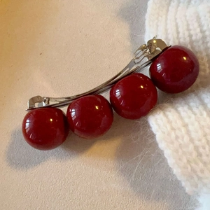 Detailed view of metal hair clip with four large glossy red pearls on fabric surface