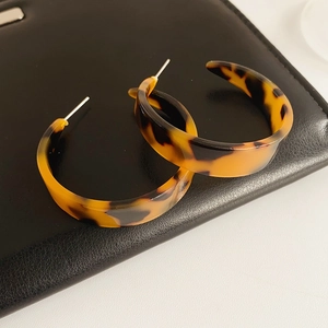 Detailed view of amber leopard print C-shape resin hoop earrings on black leather texture
