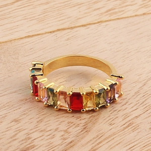 Gold eternity ring featuring multi-colored rectangular crystals on a wooden background