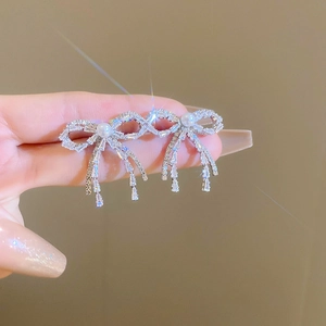 Close-up of silver bow earrings with sparkling crystals, pearls and dangling diamond tassels