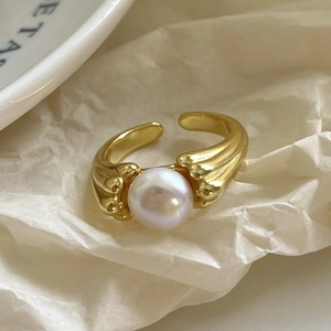 Macro detail of a wavy gold plated ring featuring a lustrous round white pearl