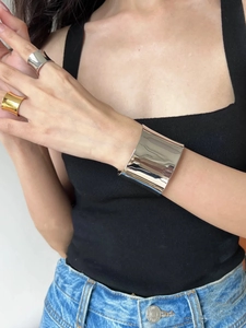 Close-up of minimalist polished silver wide cuff bracelet and bold metal rings on model