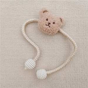 Close-up of a brown plush bear head with pearl beads on a woven beige and gold rope tie