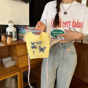 Détail d'un sac en toile jaune avec broderie papillon et bandoulière tissée violette