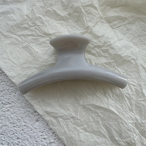 Detail of a minimalist grey PC hair claw clip on a textured beige and white background