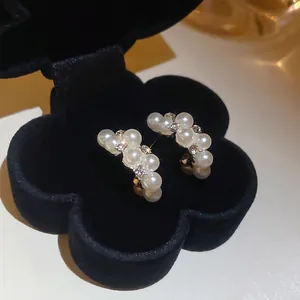 Elegant C-shaped pearl and rhinestone stud earrings displayed in a black velvet jewelry box