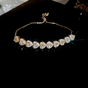 Detail of gold adjustable bracelet with sparkling heart-shaped zircon stones on dark background