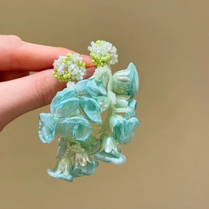 Close-up of mint green floral earrings with delicate fabric petals and beads
