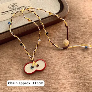 Detail shot of a handmade woven necklace featuring a bow-knot glass pendant on a fabric mat