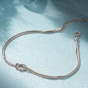 Detail of silver snake chain bracelet with a central knot charm and adjustable clasp