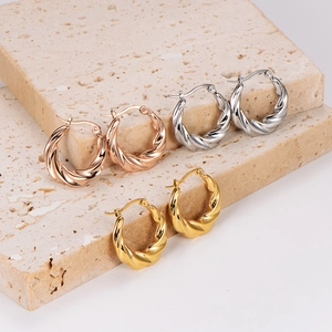 Three pairs of twisted hoop earrings in silver, gold, and rose gold on a stone base