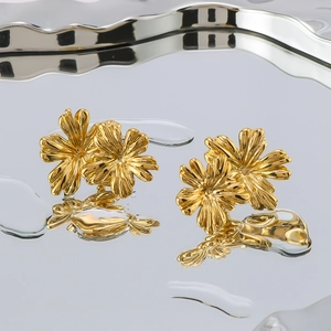 Polished 18K gold-plated double floral stud earrings on a rippled mirror surface
