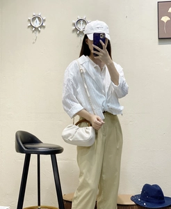 Detail of white pleated cloud bag with round wood handle and adjustable shoulder strap