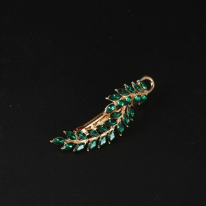 Detail of vintage gold leaf hair clip with marquise-cut green crystals on black background