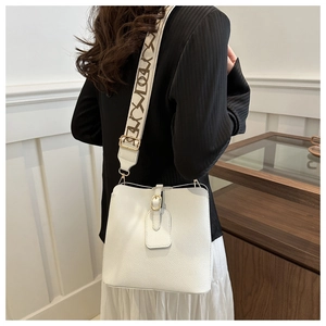 Detail of white lychee leather bucket bag with wide printed strap and gold hardware