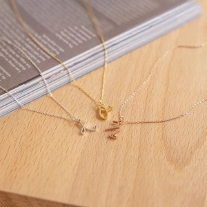 Detailed shot of initial necklaces in silver, gold, and rose gold on a wooden surface