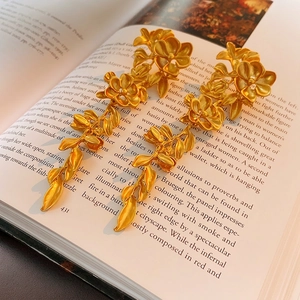 Long gold flower leaf tassel earrings displayed on an artistic open book background