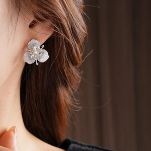 Close-up of elegant flower stud earring with translucent petals and a pearl on ear
