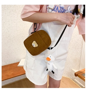 Close-up of brown corduroy crossbody bag with bear embroidery and white duck plush charm