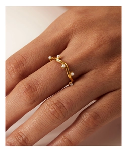 Close-up of wavy gold ring featuring white pearl embellishments worn on a hand