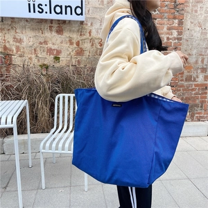 Blue canvas tote bag with woven inner check pattern and black label on casual model