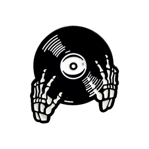 Skeleton hands holding a black vinyl record enamel pin in polished metal finish