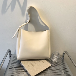 Minimalist beige leather tote bag with wide shoulder strap displayed on metal stand