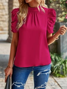 Outdoor shot of a rose red short-sleeved blouse with puff sleeves and pleated high neckline