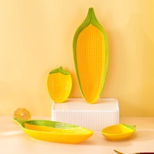 Detail view of yellow corn shaped ceramic plates with green leaves on a textured stand