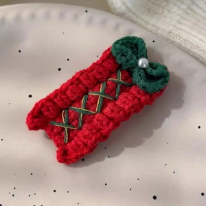 Detail of red knitted Christmas hair clip with green bow and pearl accent on a plate