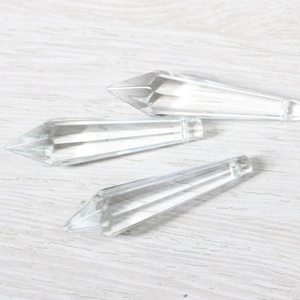Macro view of three faceted crystal prism pendants on a light wood surface texture