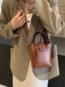 Retro brown leather mini bucket bag with woven charm, styled on a beige blazer