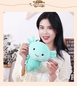 Close-up of mint green axolotl plush toy with soft gills held by a person in cozy home