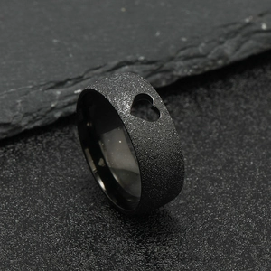 Close-up of black matte stainless steel ring with laser-cut heart pattern on a dark rock