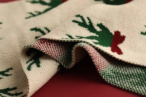 Close-up of beige knitted scarf featuring green reindeer patterns and red hem stitching