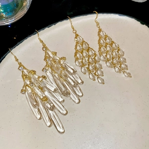 Detailed view of gold drop earrings with clear faceted beads on a white textured plate