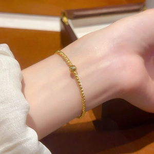 Detailed macro of 24K gold-plated beaded bracelet with engraved cylinder charm