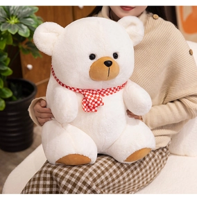 Close-up of a soft white teddy bear with a red checkered scarf held in a home setting