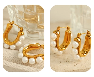 Detailed close-up of golden U-shaped earrings with white pearls on elegant fabric