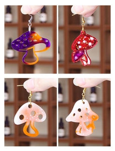 Macro display of four gradient mushroom resin earrings held by hand to show details