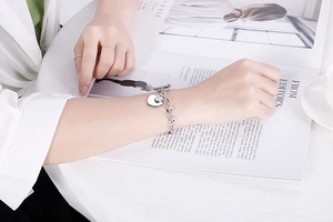 Silver stainless steel heart bracelet with OT toggle clasp worn by a model over a magazine