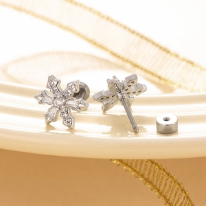 Silver snowflake earrings with zircon stones on a ceramic plate with golden ribbons