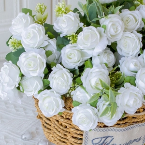 Close-up of white silk roses and green leaves in a woven basket with a flowers tag
