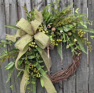 Rustic botanical wreath with green leaves, berries, and checkered bow on wood fence