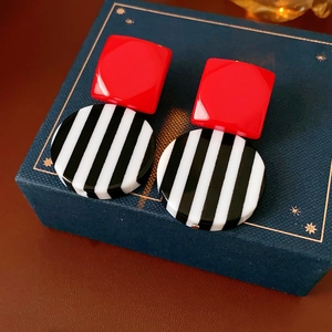 Macro detail of red square and black white striped resin earrings on blue textured box