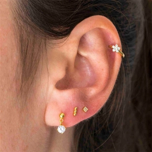 Macro view of gold flower ear cuff and zircon stud earring set on a female model
