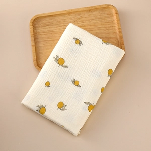 Close-up of a folded cotton muslin baby swaddle with yellow lemon prints on a wooden tray