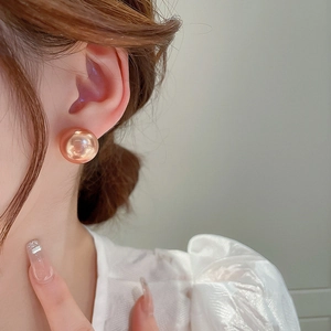 Gros plan de boucles d'oreilles boules dorées champagne sur modèle au fini métal brillant